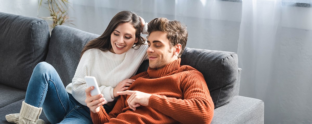 Ungt par i en soffa ser på mobiltelefonen 