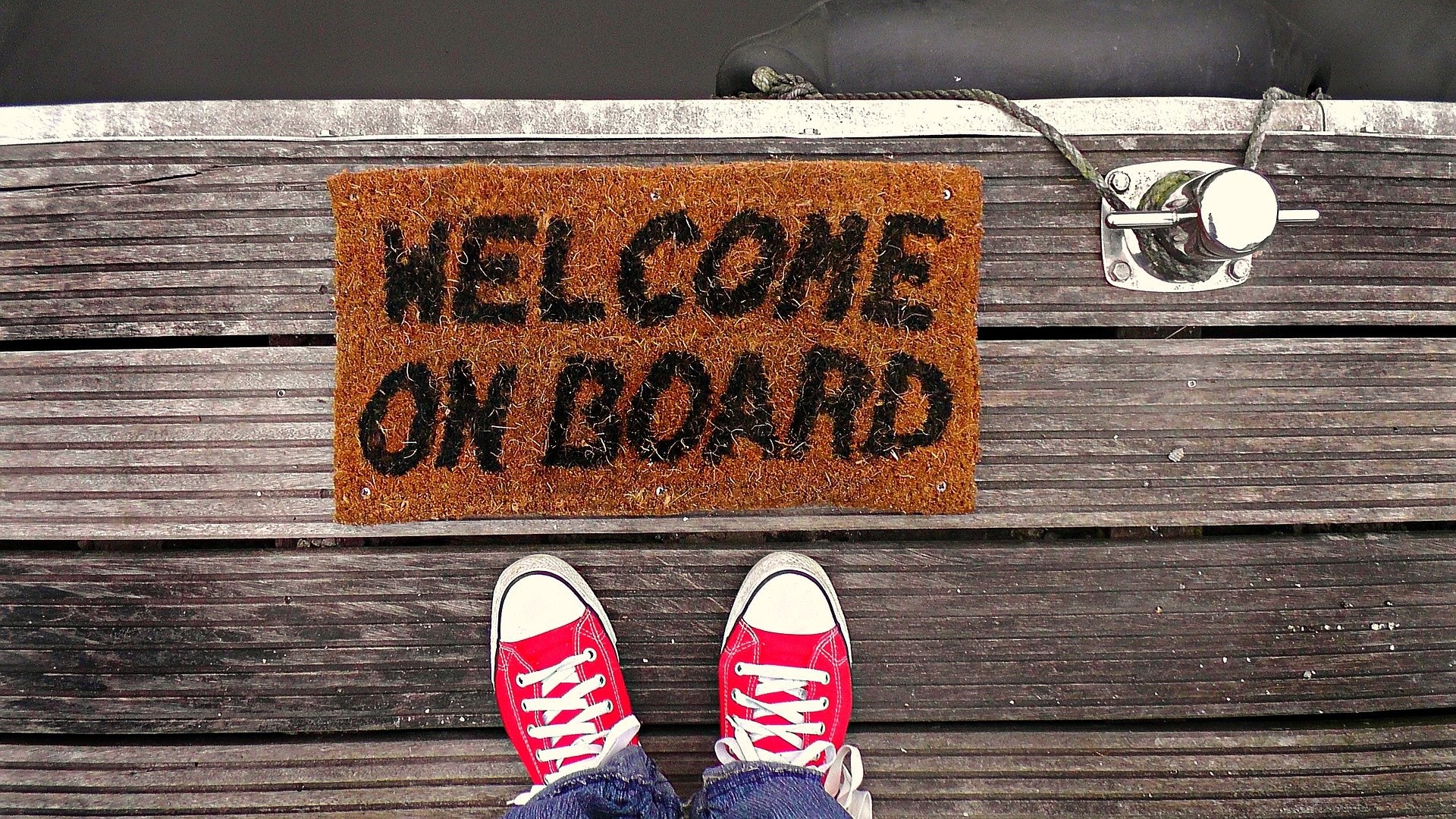 Dörrmatta med texten welcome on board och ett par röda sneakers