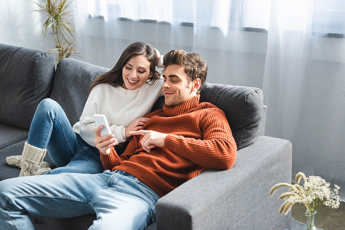 Ungt par i en soffa ser på mobiltelefonen 