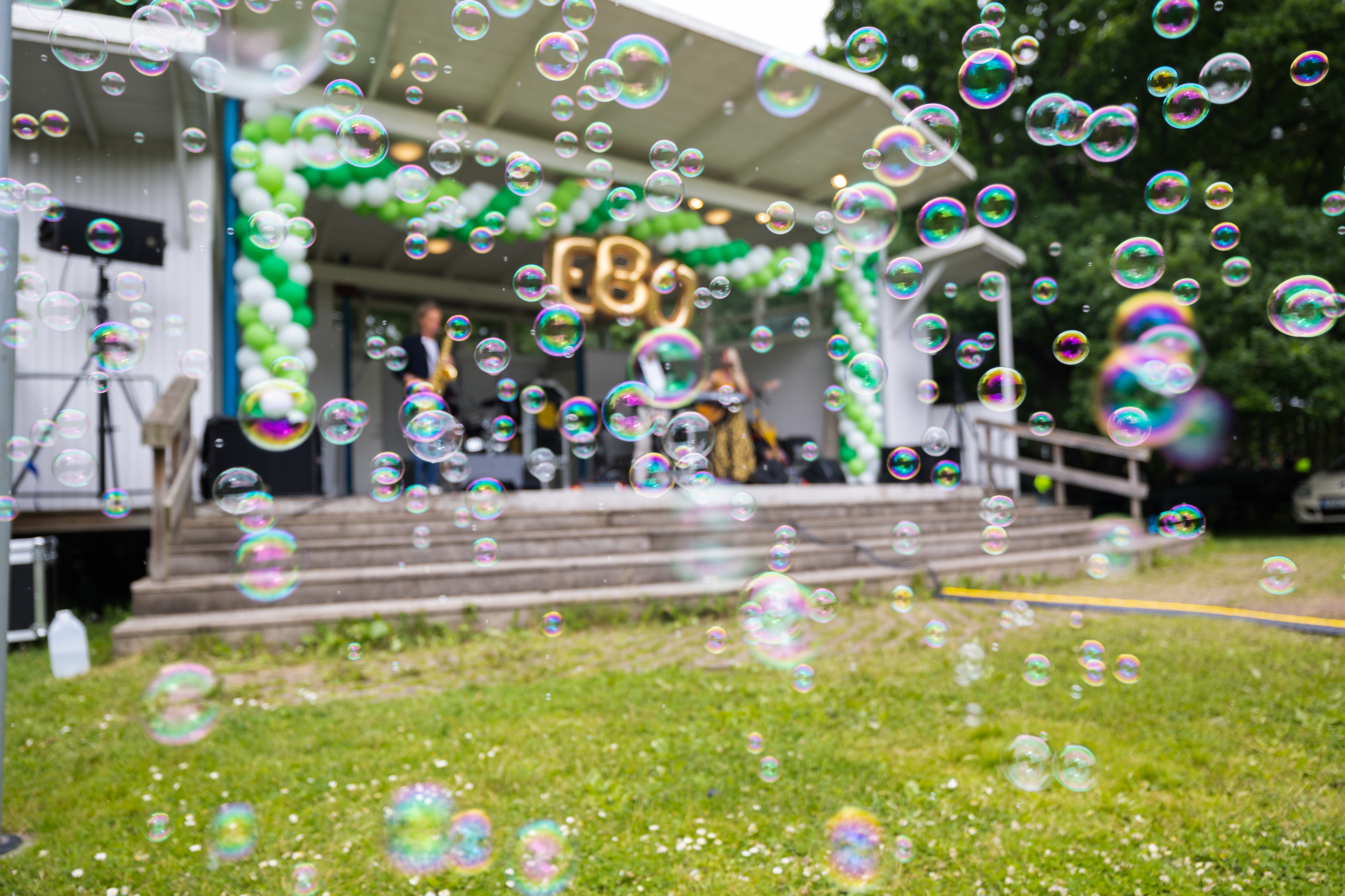 Ballonger och såpbubblor framför en scen med guldballonger med texten EBO.
